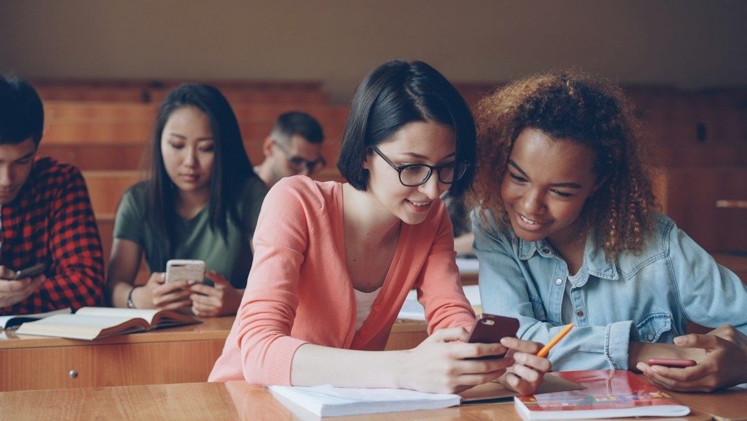 Lernende prüfen gemeinsam Smartphone-Inhalte in einem Klassenraum